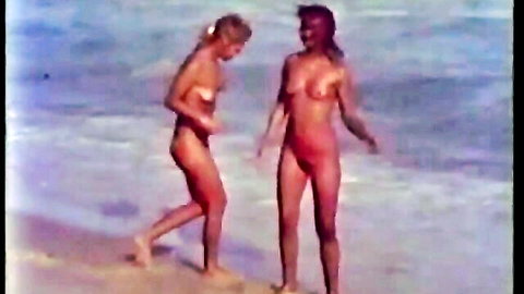 Hot blonde and brunette topless on beach in classic porn video