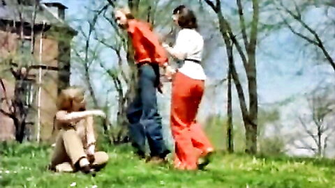 Vintage retro women in orange pants restrain handcuffed man outdoors teasing threesome