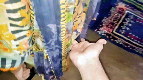 Pale hand reaching out in front of colorful hanging sarees and fabrics in amateur room
