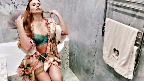 Sexy redhead MILF in green lace bra and panties poses seductively on bathtub edge