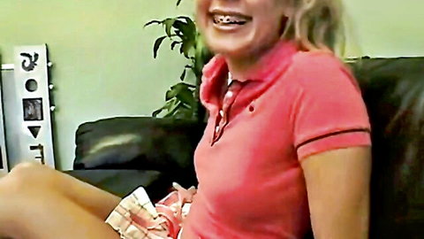 Smiling blonde teen with braces in pink polo shirt and short skirt legs spread on couch