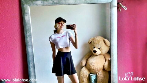 Lola Lohse cute selfie in white crop top, black skirt, and cap with teddy bear