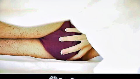 Woman's pink-nailed hand tugging down hairy man's purple underwear bulge on bed