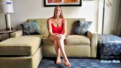 Melanie Hicks in red tank top and shorts, sitting teasingly