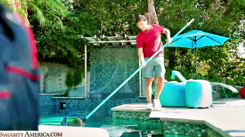 Hot pool boy in red shirt skimming turquoise pool poolside with blue umbrella