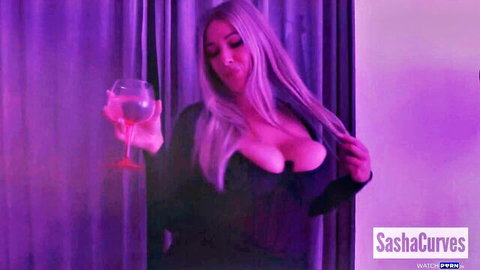 SashaCurves curvy blonde in low-cut black dress, holding pink cocktail seductively