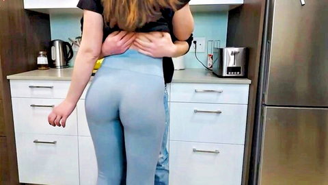 Curvy girlfriend in tight blue leggings hugged from behind by boyfriend in kitchen
