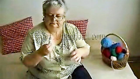 Mature granny with glasses knits yarn using needles solo on couch