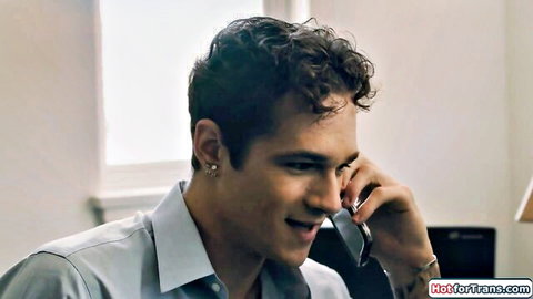Young curly-haired brunette man smiling while talking on phone in office shirt