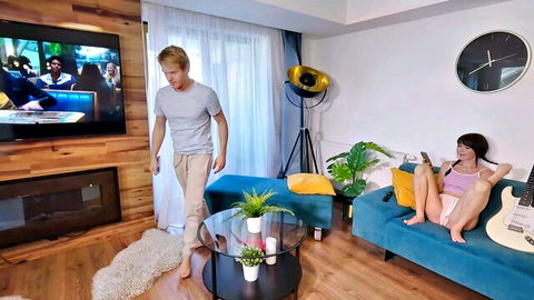 Blonde guy approaches petite Asian step-sis lounging on sofa in pink top and shorts