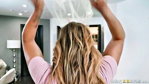 Muscular blonde in pink top raises sheer white veil over head from behind