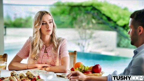 Blonde woman in pink cardigan chats intimately with handsome man at poolside table