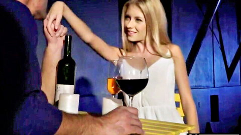 Blonde girlfriend in white dress smiles while holding wine glass as boyfriend caresses her arm romantically