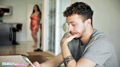 Tattooed hunk sits pensively at table while busty brunette in red lingerie teases from behind glass door