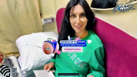 Smiling brunette in green hoodie sits teasingly on purple bed