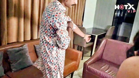 South Asian man in colorful patterned shirt standing in luxury living room with leather couches