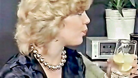 Vintage blonde in satin top with pearl necklace purses lips seductively sipping yellow drink