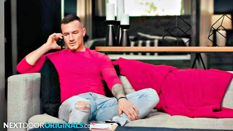 Muscular gay hunk in pink shirt and ripped jeans talking on phone on couch