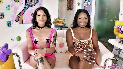 Topless Asian and ebony babes with big tits and tattoos posing seductively on pink couch