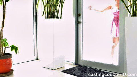 Young blonde in pink dress teasing at casting couch door holding white top