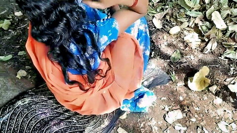 Sexy Indian woman in orange saree sitting in wild jungle surrounded by leaves and dirt