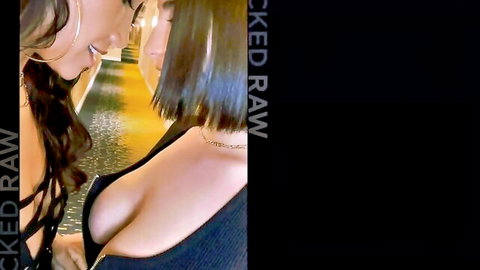 Busty brunettes in deep cleavage tops kissing intimately in yellow-lit hallway