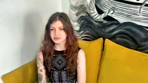 Curly redhead teen in black patterned top, tattooed arm, seductive sit