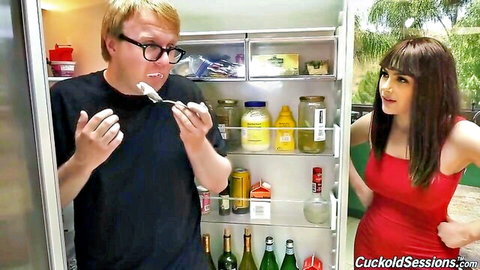 Nerdy cuckold hubby spoons food to busty brunette wife in tight red dress by open fridge