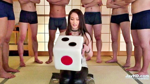 Young Japanese babe kneels holding giant dice surrounded by men in tight blue underwear