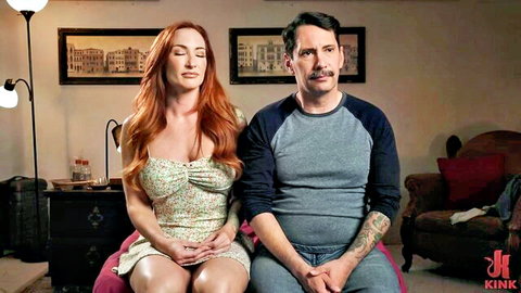 Busty redhead MILF in low-cut floral dress sits with tattooed man on Kink couch
