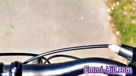 Blurry close-up of black bicycle handlebars and cables outdoors on gray path