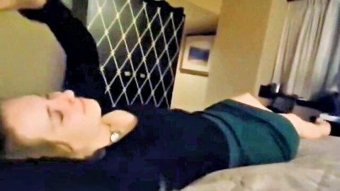 Blonde woman lying relaxed on hotel bed in black top and green skirt