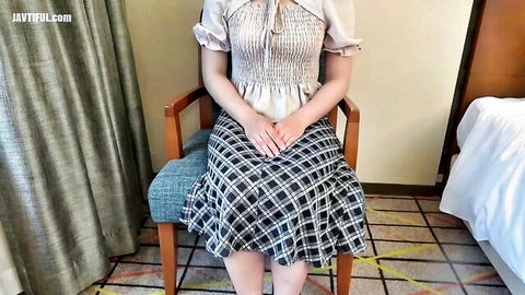 Seductive Asian babe in ruffled blouse and plaid skirt sits on chair with legs spread teasing