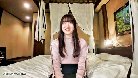 Cute Asian college girl in pink sweater and black shorts smiling on canopy bed