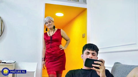 Stepmom Arwen in red dress poses seductively in doorway while young guy watches on phone