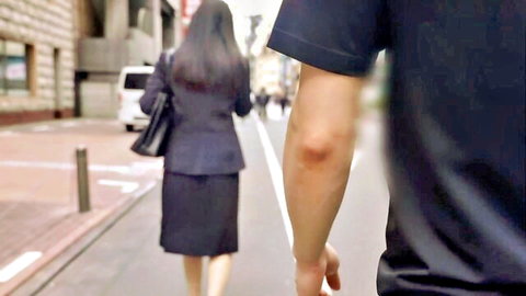 Asian businesswoman in tight skirt walking street, followed by man arm