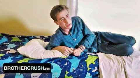 Cute young stepbrother lounging seductively on colorful shark bed in blue shirt