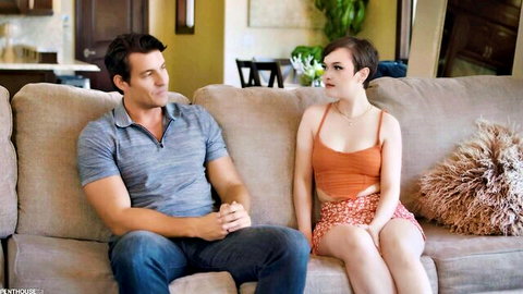 Jade Valentine in orange top and skirt with muscular man on couch