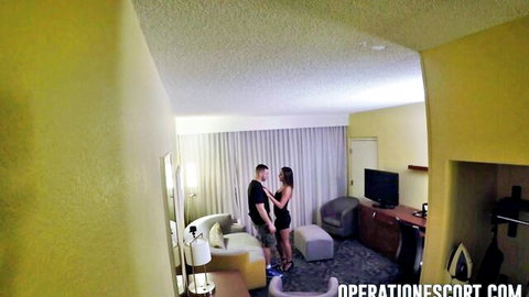 Skinny brunette escort in tight dress hugs muscular guy passionately in hotel room