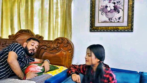 Sexy Indian woman in plaid shirt sits smirking beside bearded man lying on bed