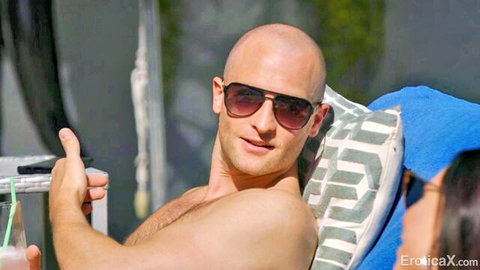 Shirtless bald hunk in sunglasses smiles giving thumbs up poolside with brunette