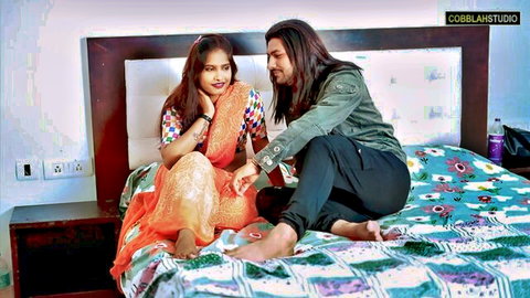 Sexy Indian woman in orange saree sits intimately with long-haired stud on bed, naughty tease