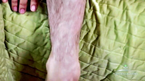Woman's hand caressing hairy man's leg on green quilted bed in natural hairy amateur video