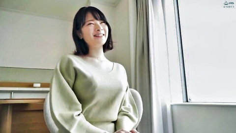 Smiling Asian woman in loose green sweater sitting indoors by window