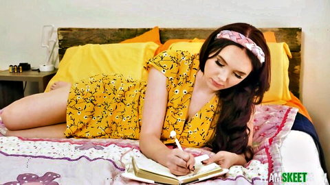 Sexy brunette in short yellow floral dress lying on bed writing in diary teasing viewers