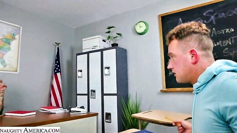 Blond guy in blue hoodie stands in American classroom with flags lockers and chalkboard