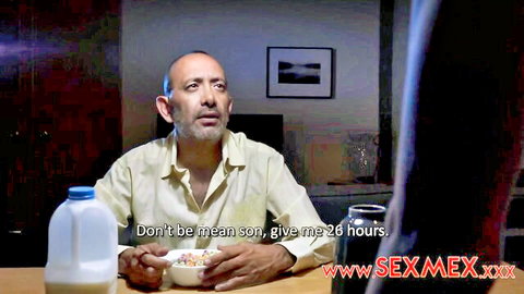 Mature balding man in yellow shirt eats cereal from bowl with milk jug at table in adult video scene
