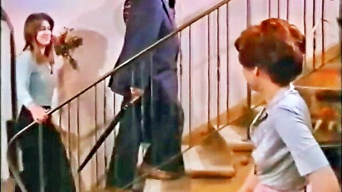 Busty brunette in blue dress holds roses on motel stairs with redhead and suited man