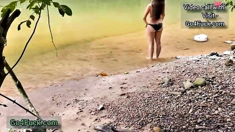 Indian girlfriend in black bikini stands in shallow river outdoors, romantic couple scene
