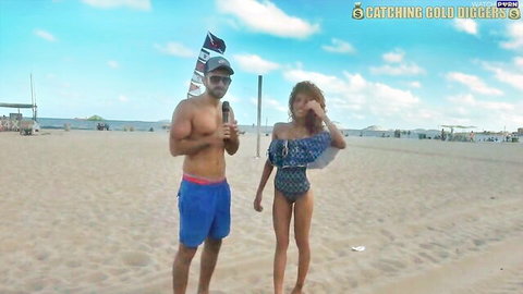 Shirtless muscular BWC guy interviews curvy Latina babe in skimpy blue bikini on sunny beach